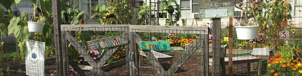 Farmingville Sprouts sign on a fence in front of a garden