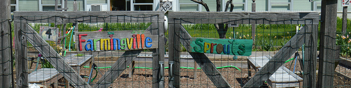 Farmingville Sprouts sign on a fence in front of a garden