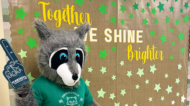 School raccoon mascot in front of Together We Shine Brighter banner